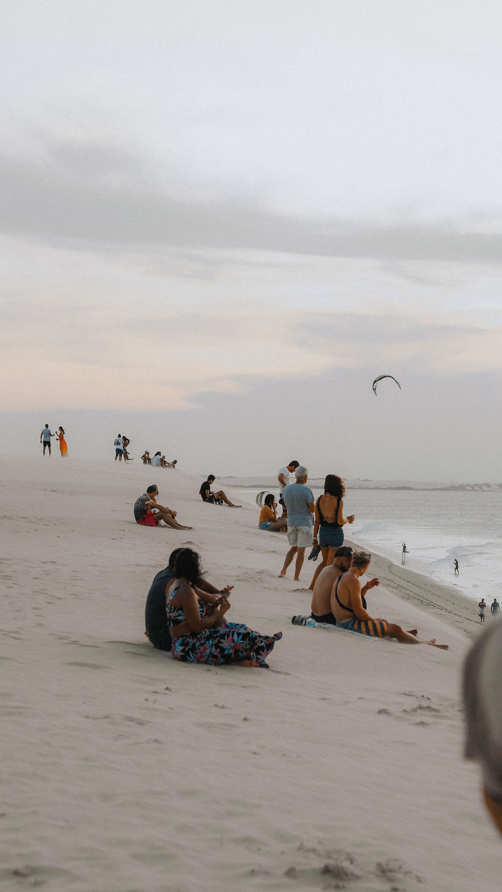 turisti su una delle dune di Jericoacoara come fossero degli spalti di un anfiteatro affacciato sul mare. un ambiente tranquillo dove la semplicità rende tutto bello. sullo sfondo un kitesurf