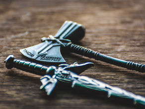 Two metallic mini weapons, an axe, and a sword, on a wooden surface. Text reads "Thor" and "Avengers Infinity War."