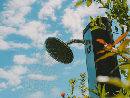 An outdoor shower head running in front of a sky backdrop.