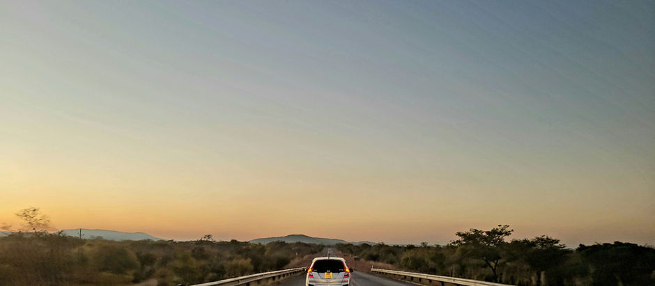 A car driving on the left hand side of the road into the sunset