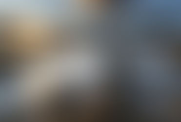 Rocky shoreline at sunset with sun rays breaking through clouds. Waves crash against rocks, creating white foamy water. Peaceful mood.