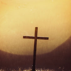 Wooden cross stands in a glowing golden sunset over a dark field, creating a solemn, spiritual mood.