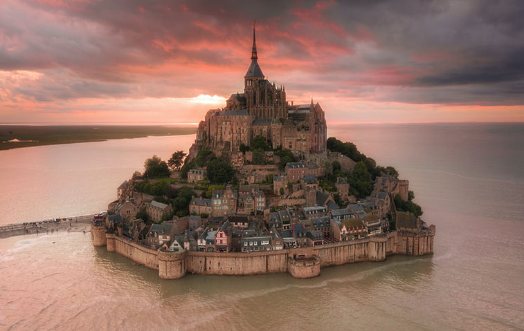 Aerial photo of Mont-Saint-Michel surrounded by high tide at sunset Photo by Unsplash © Customerly