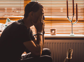 Man sits pensively, appearing stressed and concerned. The background is an orange hue.