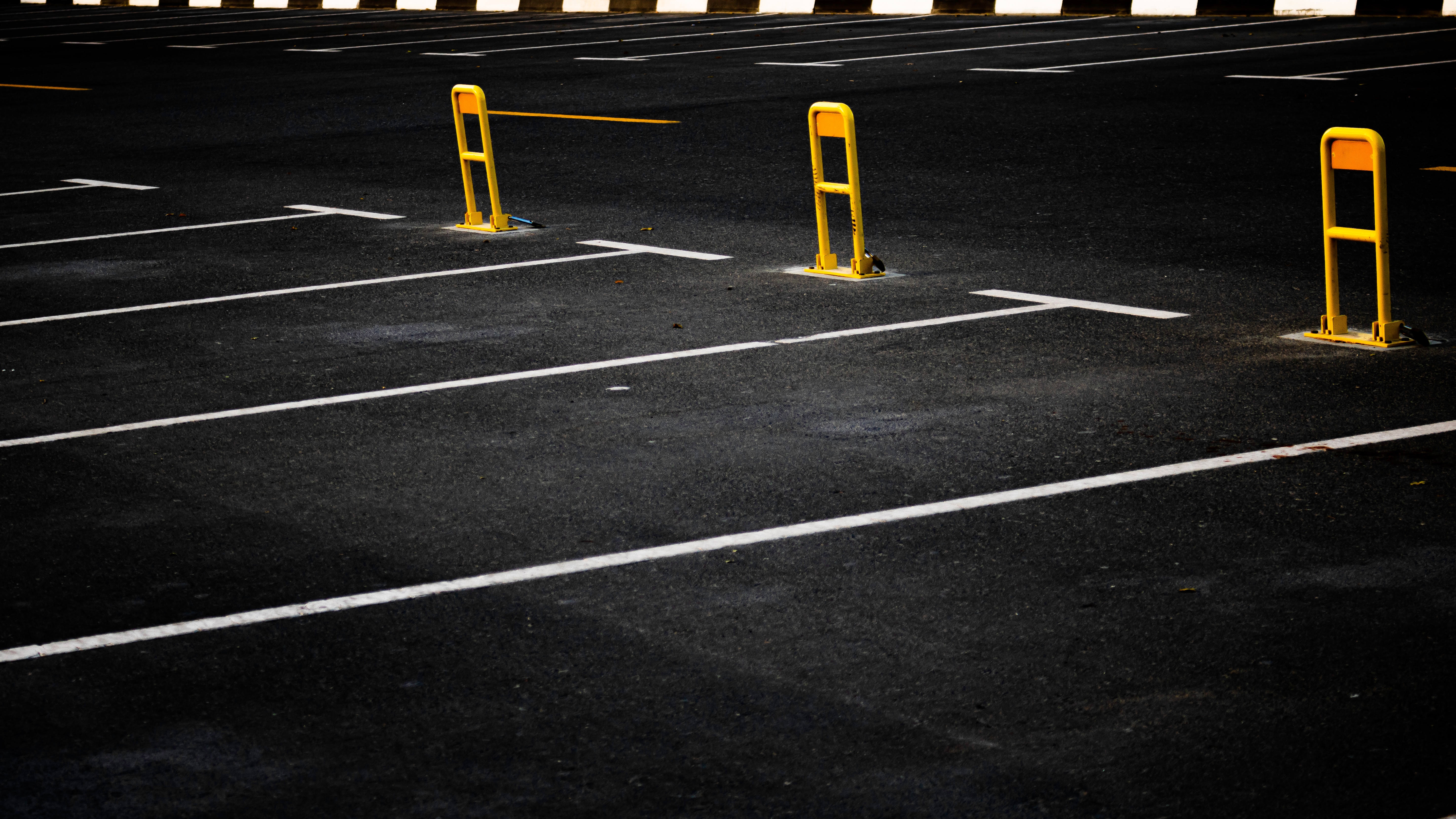 Empty parking lot with three yellow bollards and white lane markings