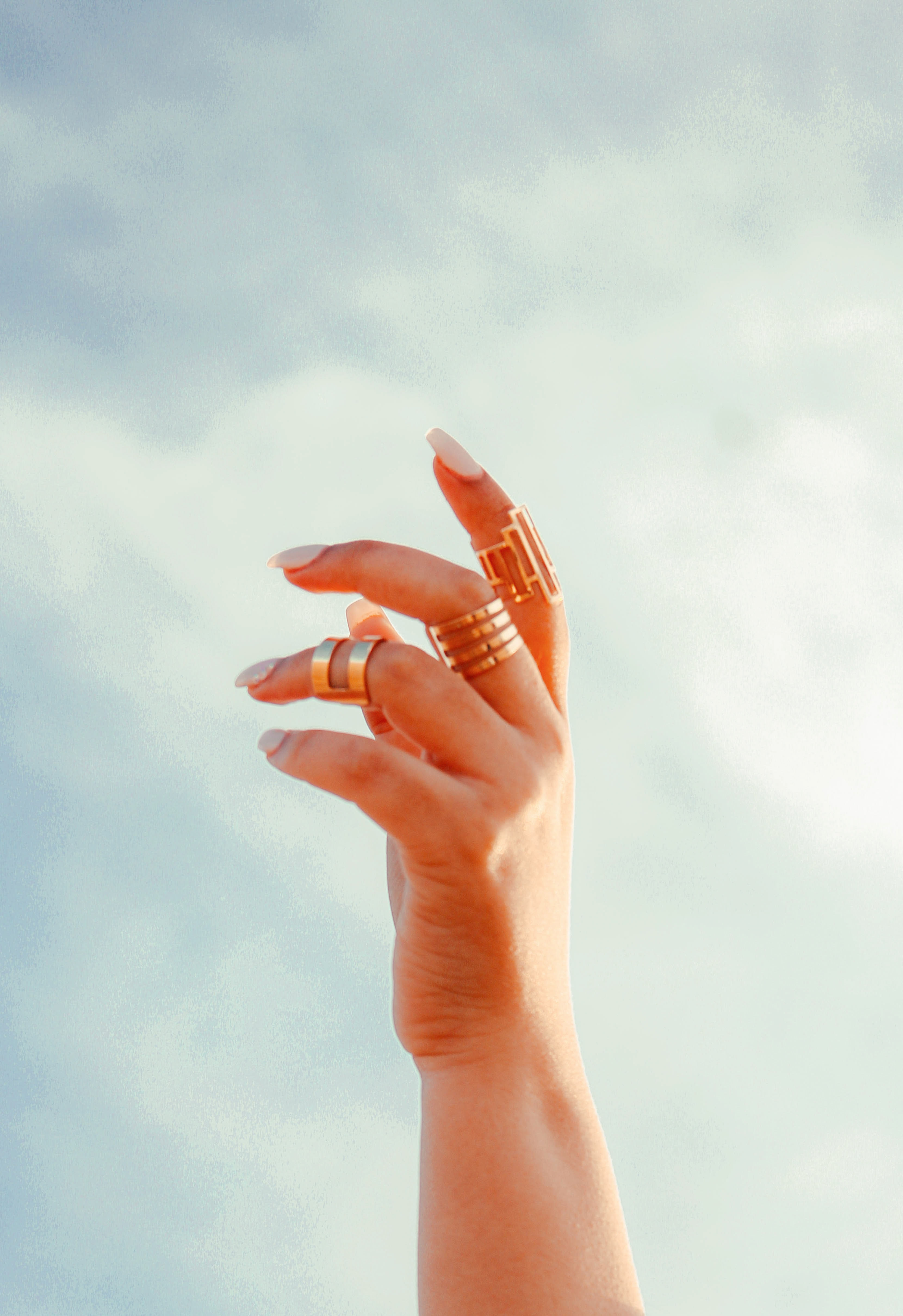 Hand model showcasing gold rings against a sky background
