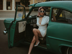 Polished woman in a neutral white dress stepping out of a vintage car, showcasing understated luxury, timeless style, and a put-together aesthetic.