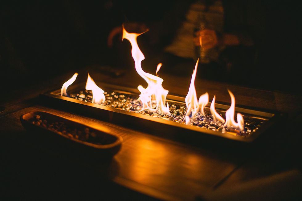 Warm, cozy setting with a tabletop fire feature surrounded by glowing stones. Soft light creates a relaxed atmosphere indoors.