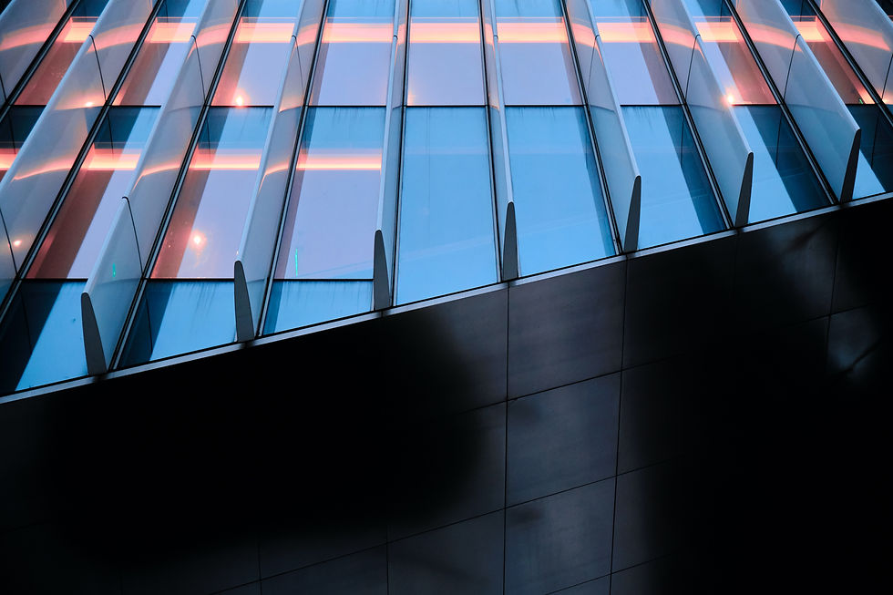 Modern building facade with glass panels, reflecting blue and pink hues. Vertical lines create a symmetrical pattern. No text visible.