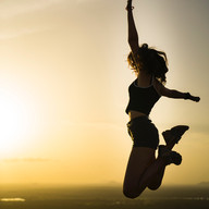 junge, schlanke Frau die mit offenen Armen hochspringt