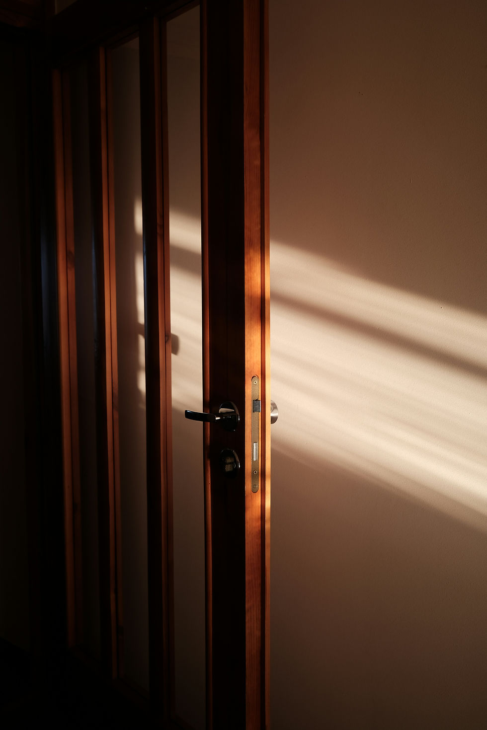 Halfopen houten deur met warm zonlicht als symbool voor veiligheid, vertrouwen en een eerste stap bij moeite met aanraking.