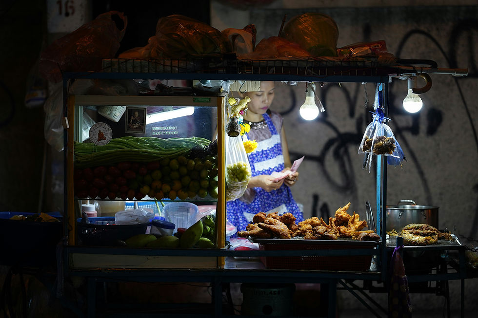 Bangkok street food stall at night with fried chicken and fresh vegetables, woman counting money