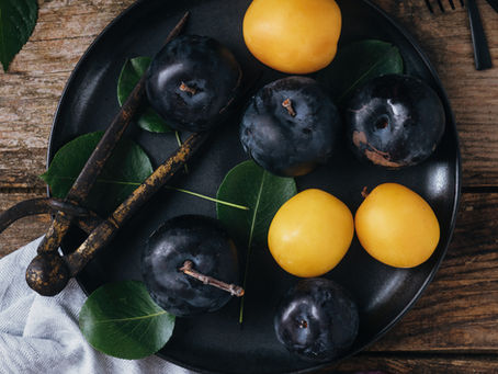Fresh purple and yellow plums on a plate, celebrating seasonal late summer fruits