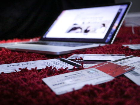 Laptop on red carpet with several scattered credit cards in focus. The screen shows a blurred webpage, creating a mysterious mood.