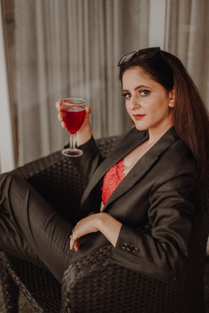 A stylish woman in a dark blazer holding a glass of red wine while relaxing in a wicker chair during a BACCO event.
