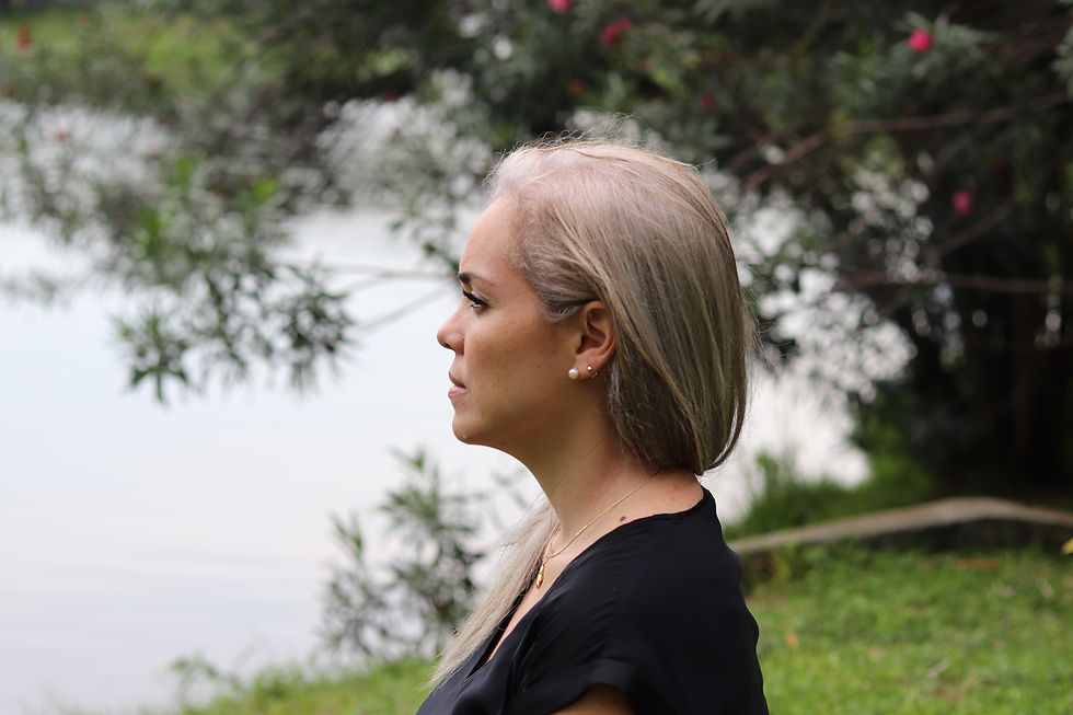 Profile of a middle-aged woman with long hair looking contemplative, wearing a black top. Background shows greenery and a calm lake.