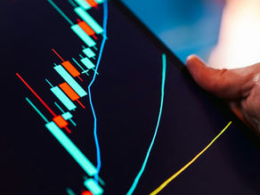 Tablet displaying a colorful candlestick chart with a hand touching the screen. Blurred blue background suggests a financial setting.