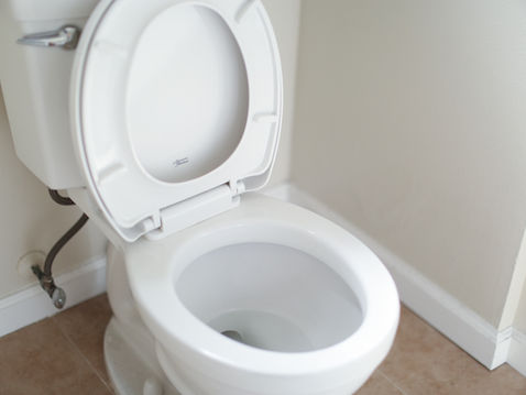 White toilet with lid up in a clean bathroom corner, beige tile floor and walls, calm minimalist scene