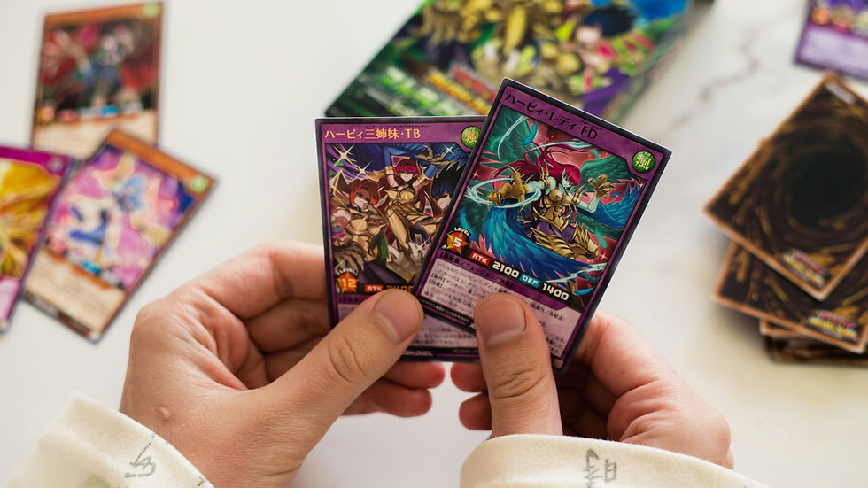 Hands holding two colorful trading cards with Japanese text, surrounded by more cards on a white surface. Bright and focused setting.