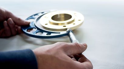 Hände halten blaue und goldene Metallteile, Markierung mit Stift. Präzisionsarbeit und Qualität in der Fertigung.