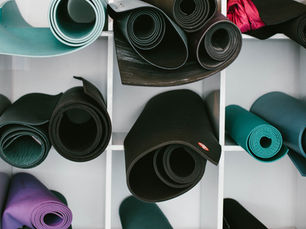 Rolled yoga mats in various colors are neatly arranged in a white cubby shelf. Bright hues of teal, black, purple, and pink dominate.