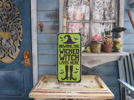 Vintage porch sign reading “Beware, the wicked witch lives here” displayed outside a charming home with plants and rustic decor.