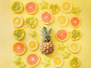 Sliced citrus fruits, starfruit, and a whole pineapple arranged symmetrically on a bright yellow background, creating a vibrant pattern.