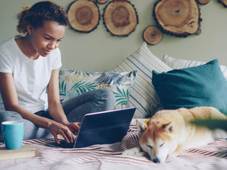 femme assise sur son lit faisant des recherches sur un ordinateur avec son chien dormant à ses côtés