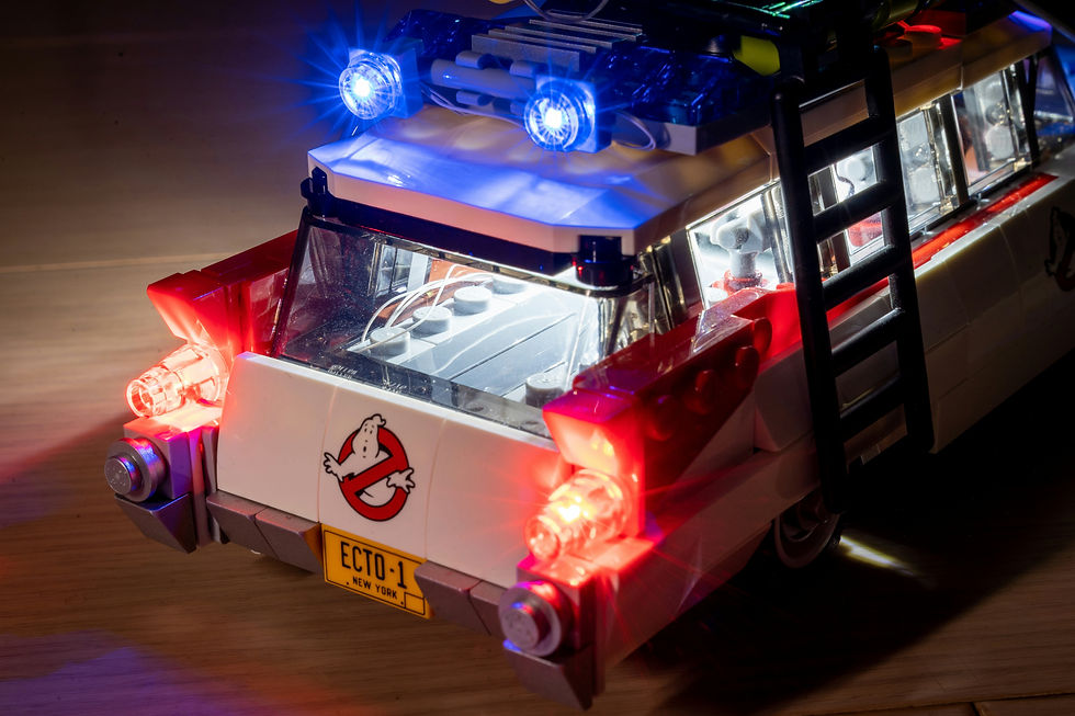 LEGO Ghostbusters Ecto-1 model with flashing blue and red lights on a wooden surface, glowing in a dark room.