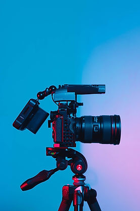 A camera used for video production sits in front of a blue / pink screen in the background.