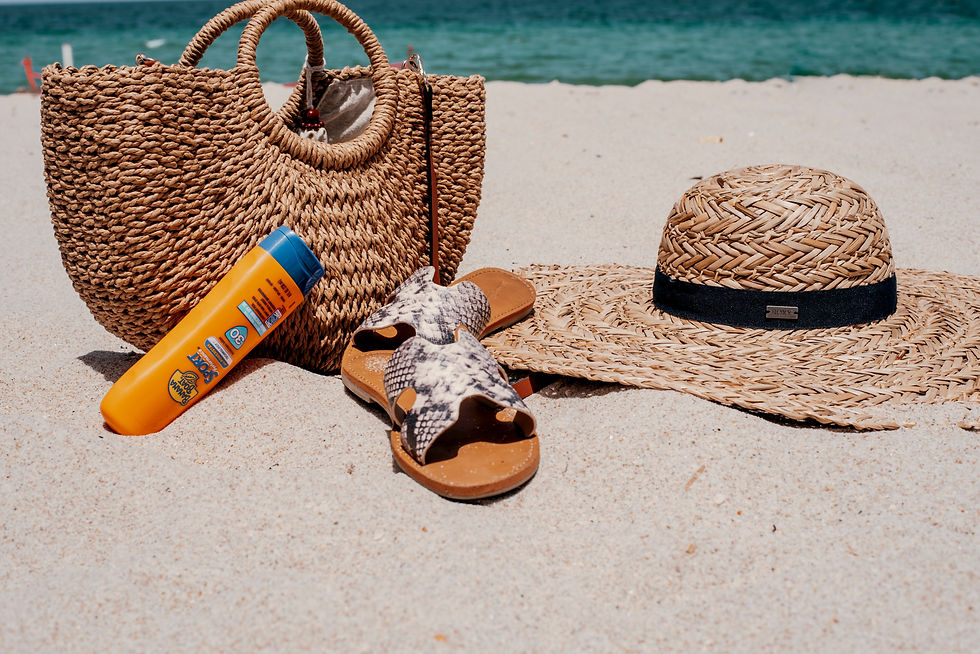 Beach scene with a straw bag, hat, sandals, and sunscreen on sand. Blue sea in background. Relaxed, sunny vibe.