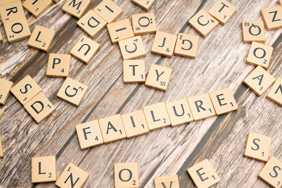Scrabble tiles spell FAILURE amid scattered letter tiles on a rustic wood tabletop, creating a tense, defeated mood.
