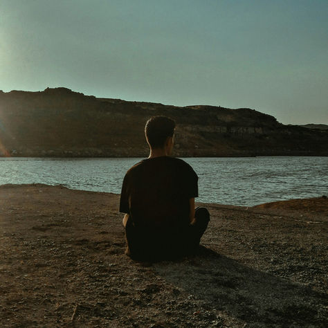 A person sitting quietly alone by a lake at dusk, illustrating stillness and embracing vulnerability