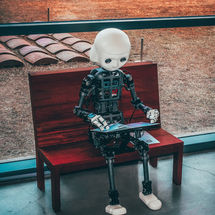 Robot humanoïde assis sur un banc en train d’utiliser un ordinateur portable, illustrant l’intégration de l’intelligence artificielle dans les technologies modernes