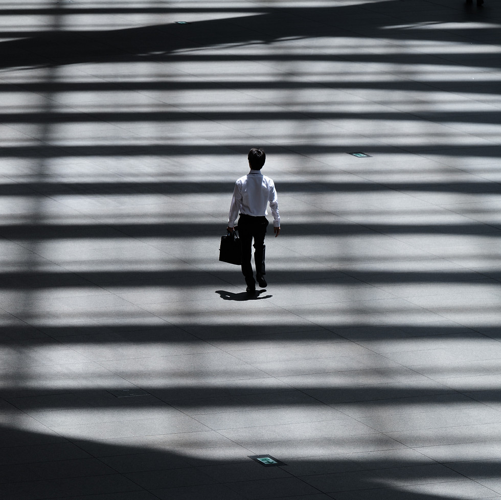 A business man stands alone staring up a vast staircase outside a city building