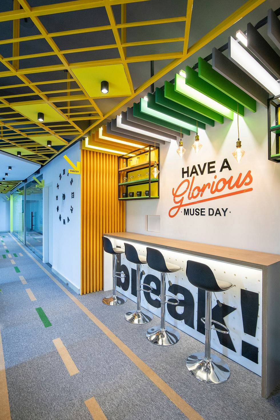 Modern office lounge with black stools, colorful ceiling, and "Have a Glorious Muse Day" on the wall. Bright, creative vibe.