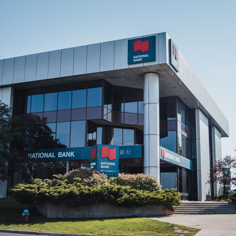 Modern bank building with reflective glass, labeled "National Bank." Surrounded by trees and greenery, under a clear blue sky.