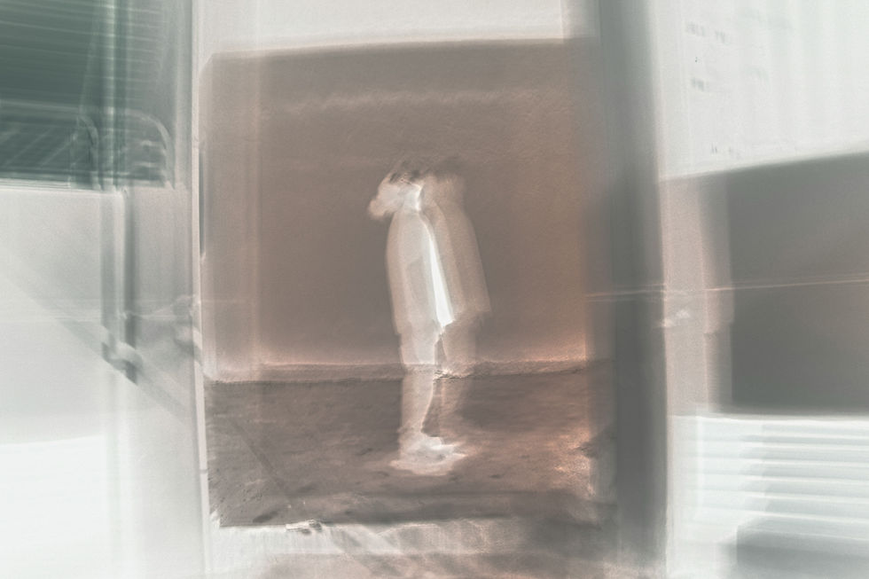 Blurred figure in a white dress stands in a doorway of a dim, hazy room with warm brown tones.