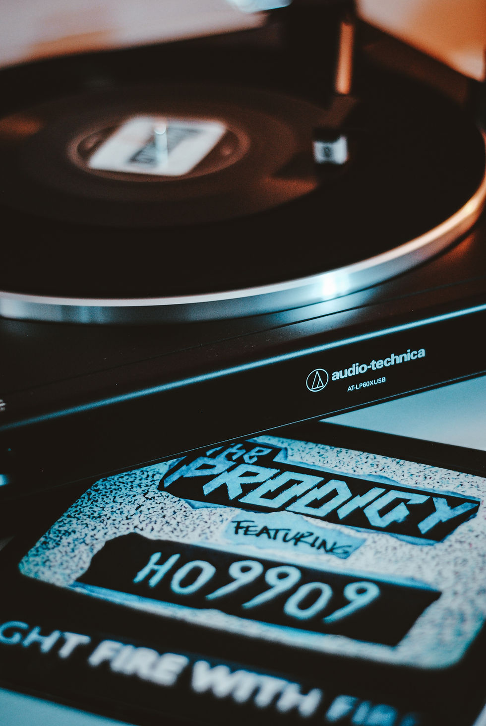 Close-up of a spinning vinyl on an Audio-Technica turntable. The record cover reads "The Prodigy featuring Ho99o9." Moody, retro vibe.