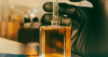 Gloved hand holding a dropper over a bottle of oil.