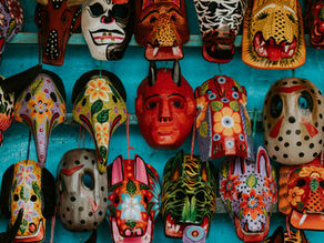 Colorful, intricately painted masks hanging on a bright turquoise wall. Patterns include flowers, spots, and animal faces, evoking vibrant culture.