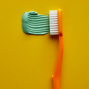 green toothpaste with an orange toothbrush on a yellow backgroung