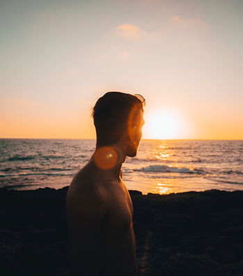 Ein Mann steht am Meer und schaut in den Sonnenuntergang