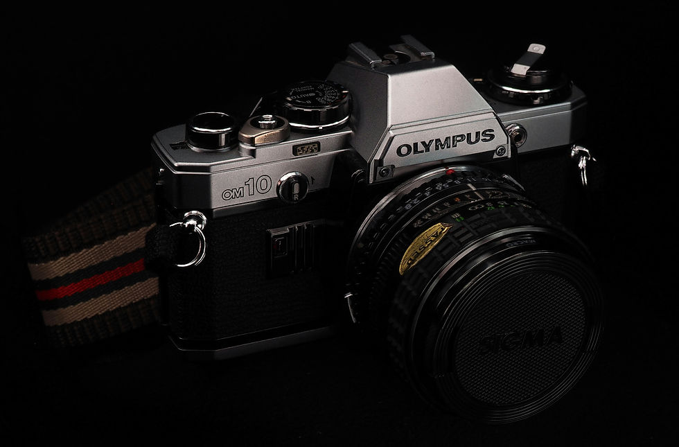 Vintage Olympus OM10 camera with a Sigma lens on a dark background. Silver body contrasts with black, evoking a classic, nostalgic mood.