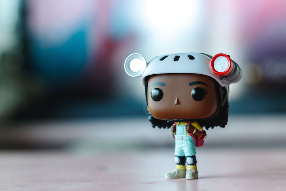Funko Pop figure of a person wearing a white helmet with goggles and overalls. Background is blurred with soft colors. Mood is playful.