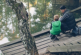 Vuxen och barn sitter på en träbrygga vid en sjö och fiskar tillsammans