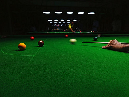 Player lining up a shot on the white cue ball at a green-cloth billiard table inside a pool club — premium billiard tables from TSports Dubai