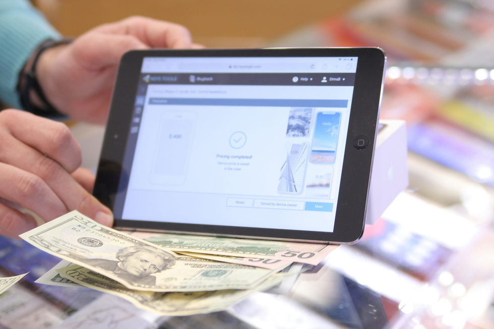 Tablet displaying "Pricing completed!" held by hand, cash on table; bright, blurry background with a tech and transaction theme.