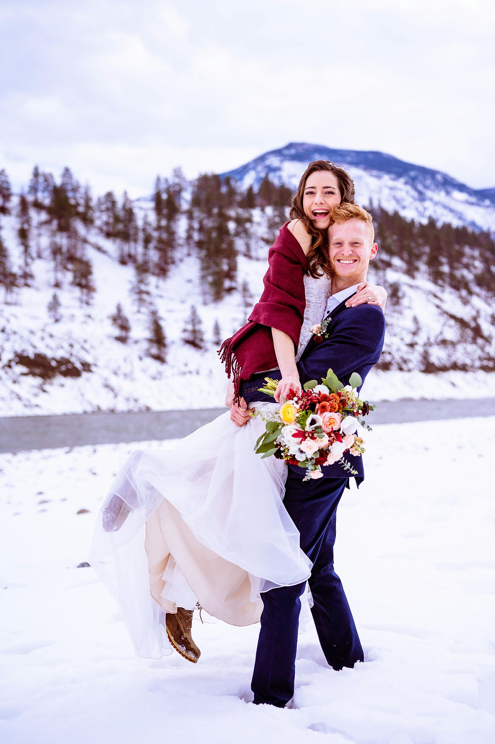 A couple in wedding attire holds each other warmly in a snowy landscape, capturing the magic of their winter wedding.