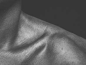 Close-up of a person's textured shoulder and neck in black and white, emphasizing skin details against a dark background.